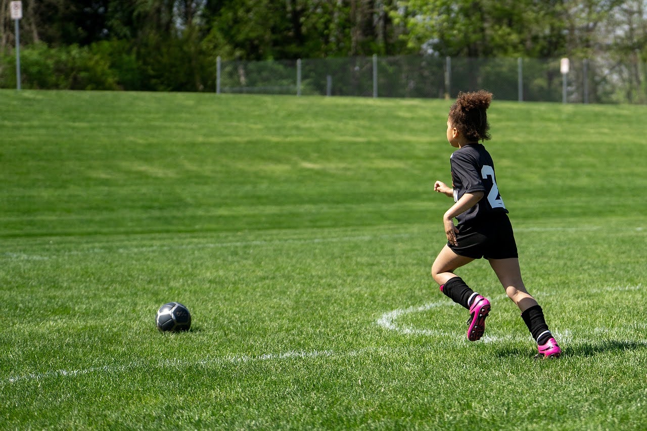 A kid running after a soccer ball.