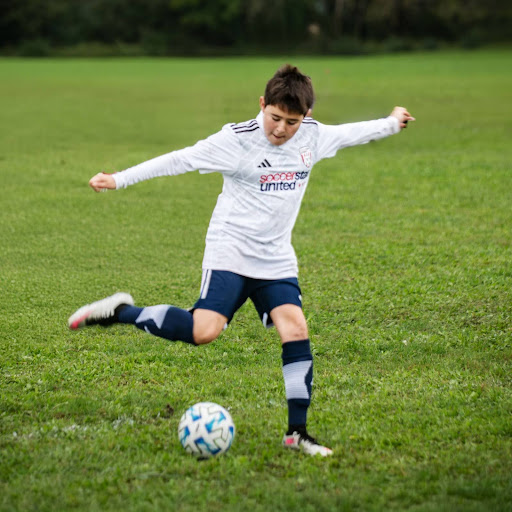 A kid in a white shirt kicking a soccer ball.